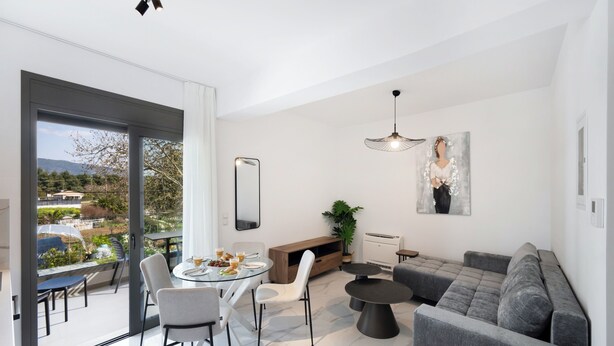 A modern living room with a grey sofa, a round dining table, and a large window offering a view of the outdoors. - Urban Nest Collection Modern CityLiving  (Lefkada)