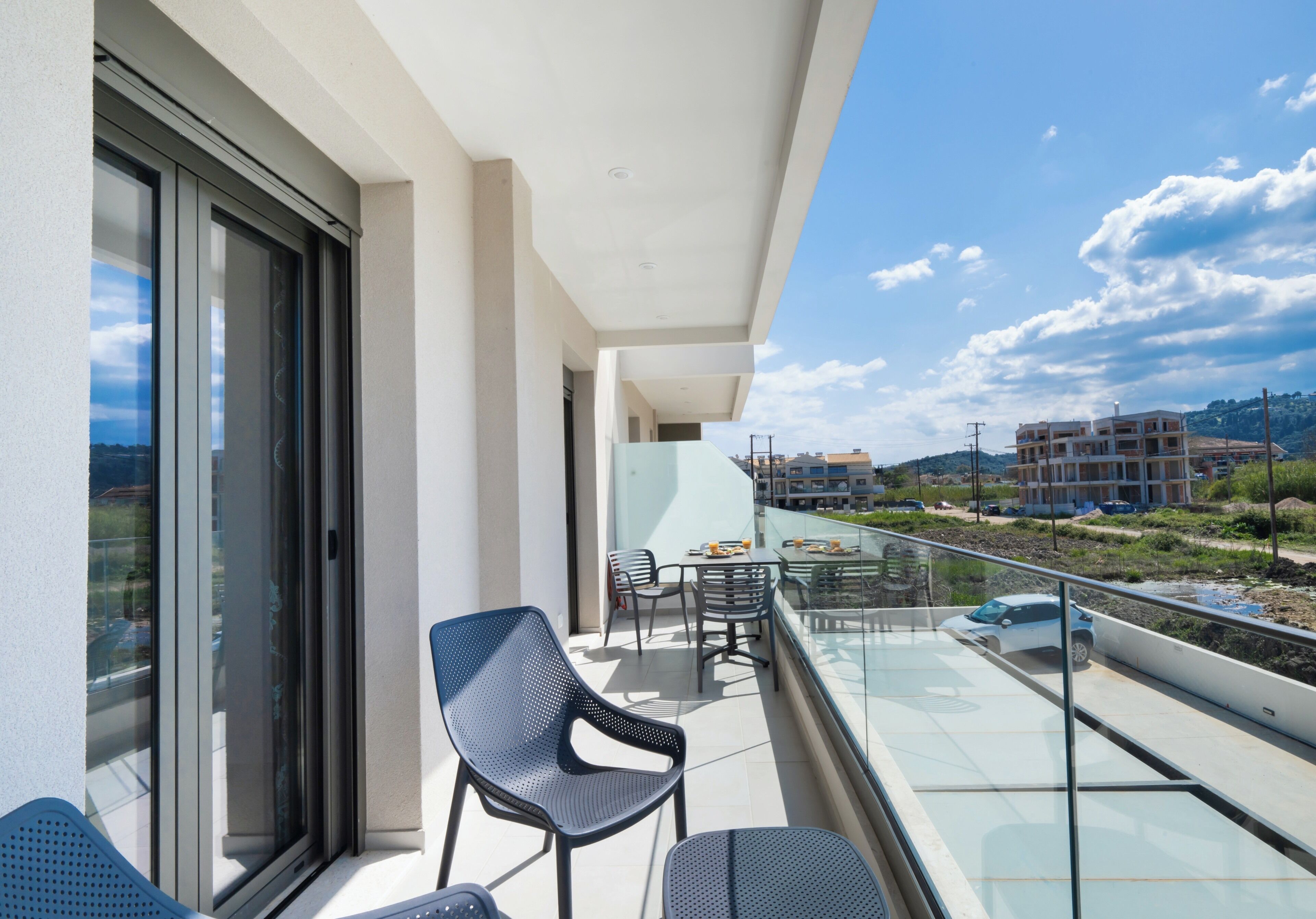 A balcony with chairs and a table, overlooking a coastal area with buildings in the distance.
