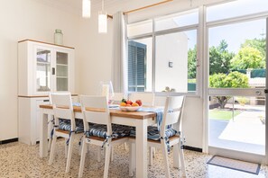 Ein Essbereich mit einem Holztisch und weißen Stühlen, einem Schrank mit Glastüren und Blick durch ein großes Fenster.
