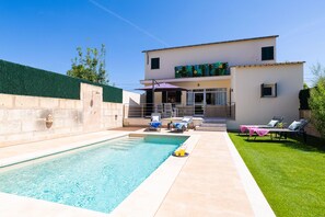 Ein zweistöckiges Haus mit Swimmingpool, einem Balkon mit farbenfrohen Kunstwerken und einer Terrasse mit Liegestühlen.