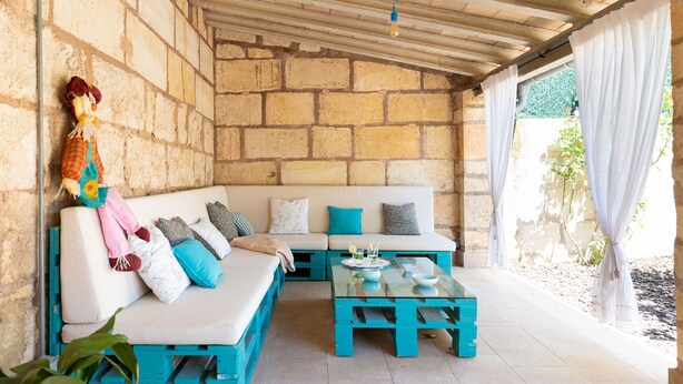 A covered outdoor seating area with a stone wall, a white sofa with blue cushions, a glass table, and a hanging decoration. - Pou de s'Alou by Rentallorca (Sineu)