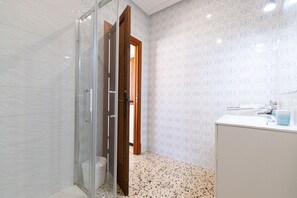 Ein Badezimmer mit Duschkabine aus Glas, einem weißen Waschbecken und Wandfliesen mit Muster.