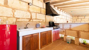 A kitchen with stone walls, a red refrigerator, wooden cabinets, a black range hood, and a countertop with a watermelon. - Pou de s'Alou by Rentallorca (Sineu)