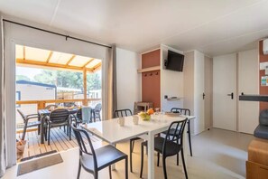 Une pièce comprenant une table à manger, des chaises, un téléviseur fixé au mur et une porte coulissante donnant sur un espace extérieur.