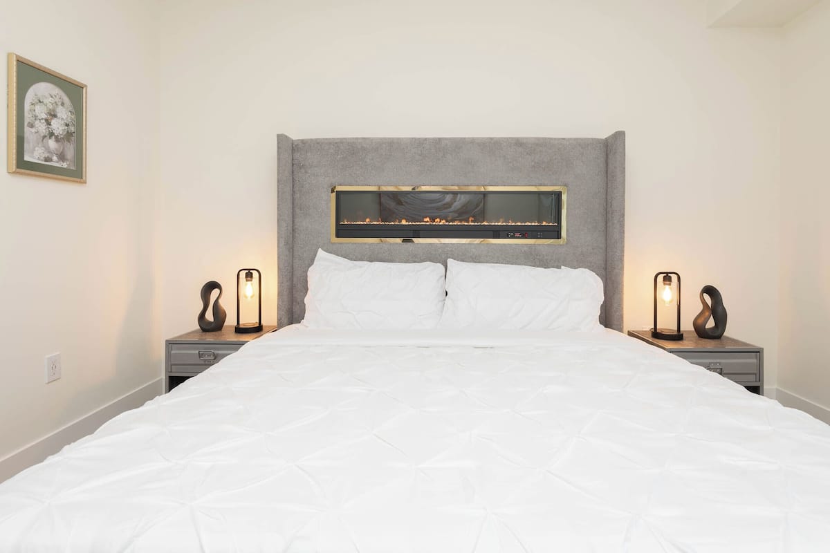 A neatly made bed with a headboard, two bedside tables with lamps, and a framed picture on the wall.