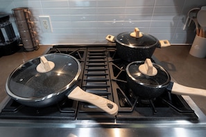 Une cuisine équipée d’une cuisinière, de deux casseroles avec leurs couvercles et d’un porte-ustensiles en bois.