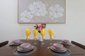 A dining table set with pink bowls, plates, and cutlery, with a vase of flowers and yellow napkins.