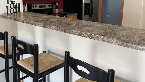 A kitchen with wooden cabinets, a stainless steel refrigerator, a microwave, and a granite countertop. There are three bar stools with woven seats. - Executive home in Private HOA near Amusement Parks. 2 Master Bedrooms - Sleeps 6 (Waterloo)