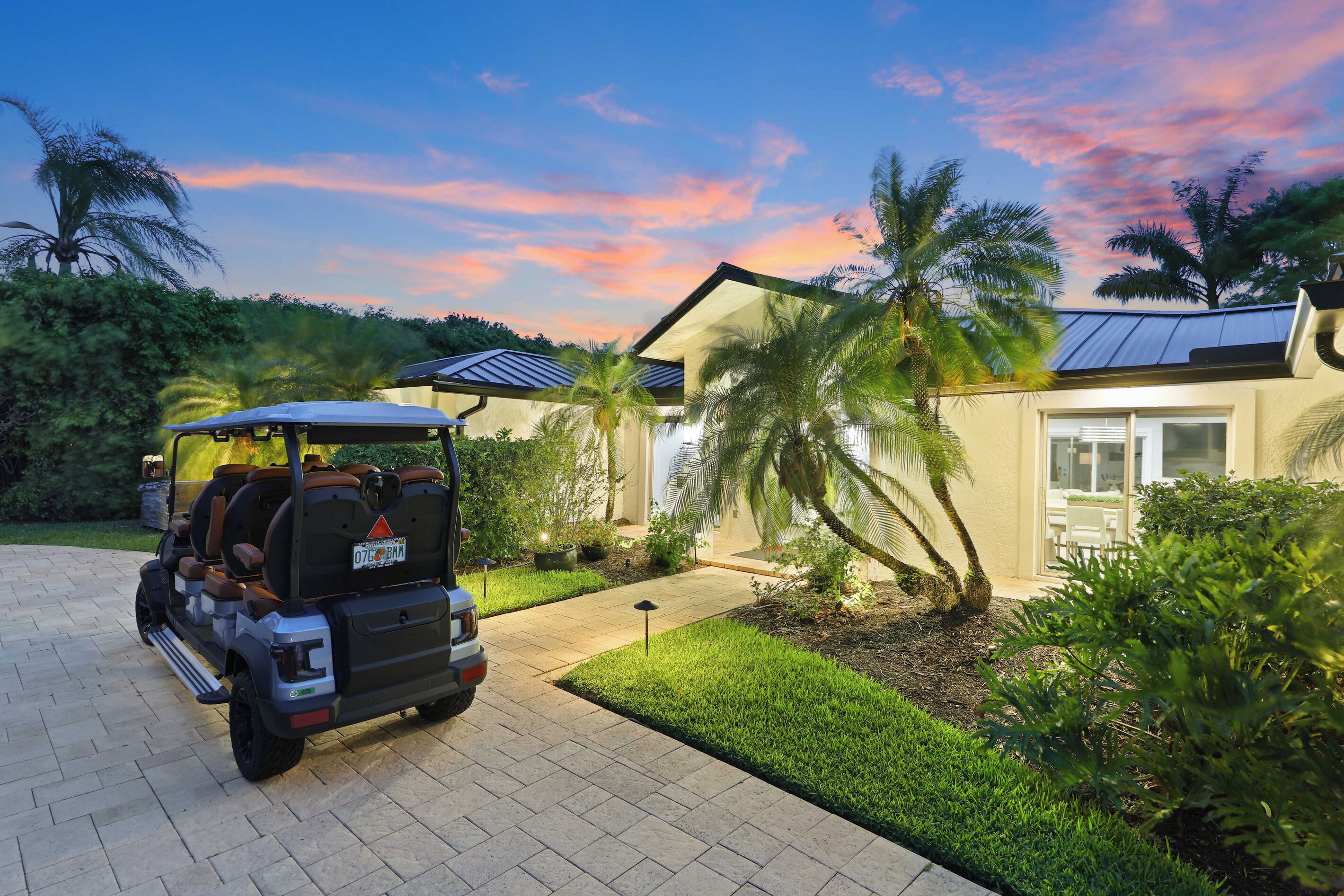 A vehicle parked in a driveway with a house and palm trees in the background.
