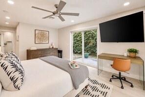 Une chambre à coucher comprenant un lit, un bureau, une chaise, un ventilateur de plafond et un téléviseur.