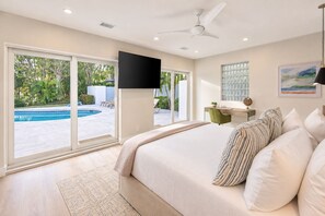Ein Schlafzimmer mit einem großen Bett, einem Schreibtisch, einem Stuhl, einem Fernseher und Blick auf einen Swimmingpool.