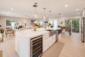 A modern kitchen with a large island, built-in oven, and a foosball table. - Direct Lake Ida Access | Sleeps 8 | Golf Cart | Heated Pool | by Delray Nightly (Boynton Beach)