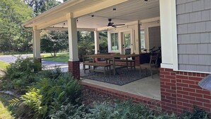 Eine überdachte Terrasse mit Tisch, Stühlen, gemauertem Unterbau und Deckenventilator.