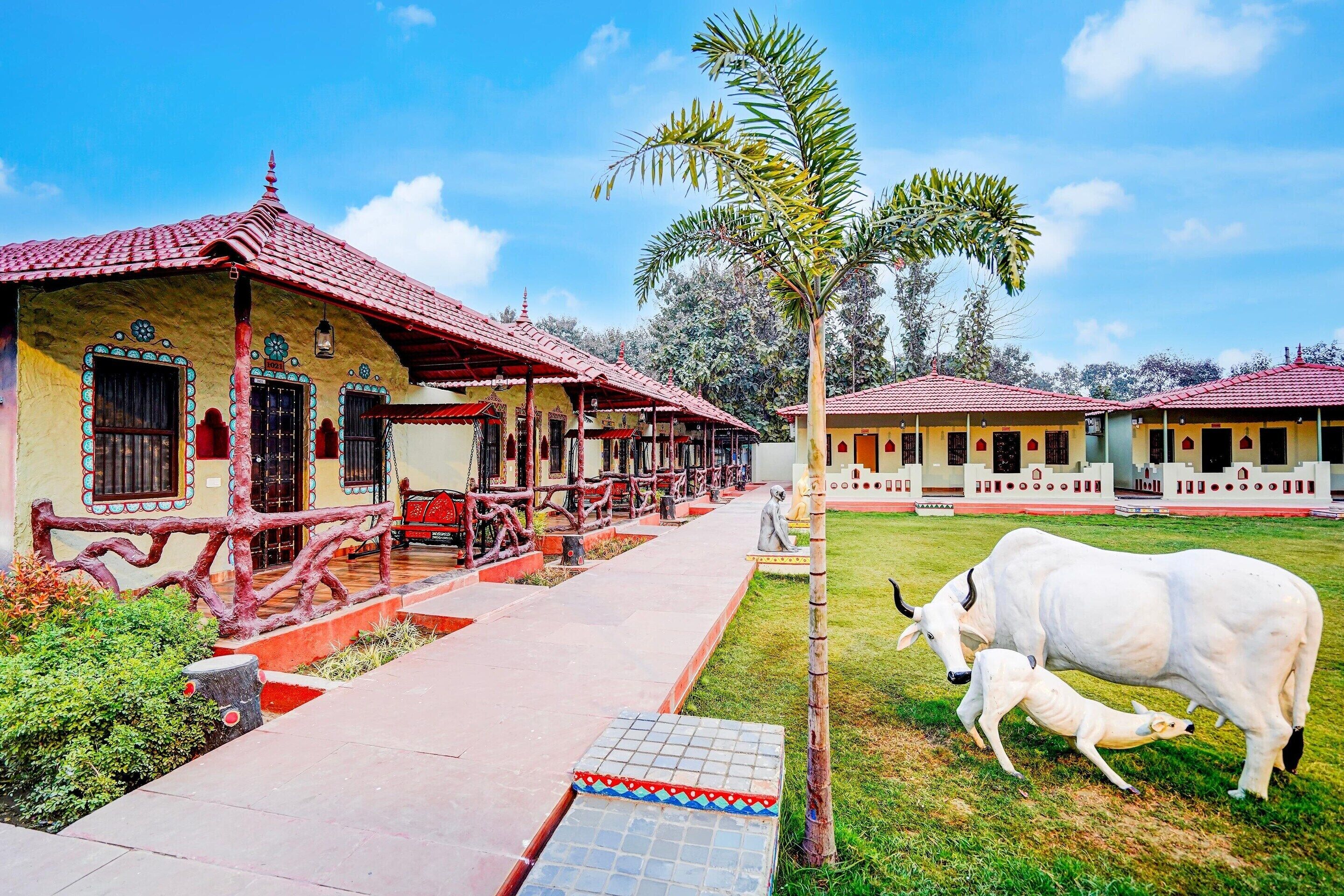 A building with a red-tiled roof, a covered walkway, and a grassy area with a cow and calf.