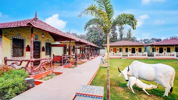 A building with a red-tiled roof, a covered walkway, and a grassy area with a cow and calf.