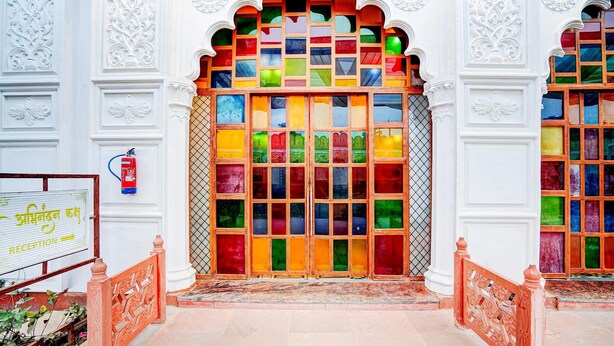 A reception area with a colorful glass door, white ornate walls, and a sign indicating the reception. - Deluxehotel Banaras Kila (Pindra)