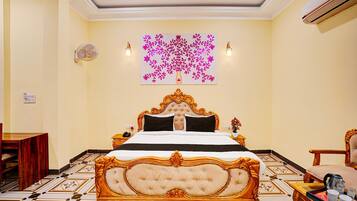A hotel room with a large bed, a wall-mounted artwork, a bedside table, a chair, and a floor with patterned tiles.