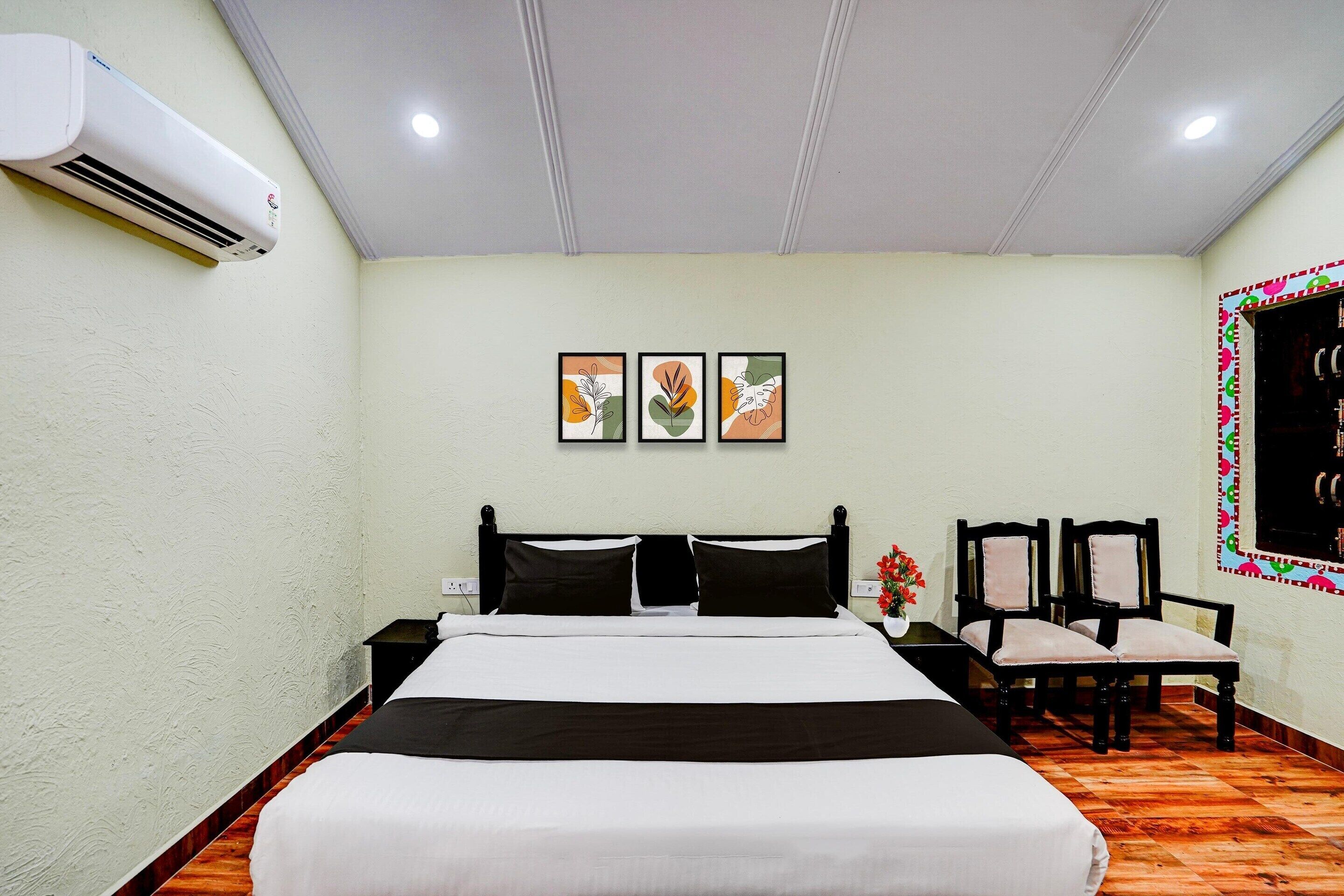 Une chambre d’hôtel comprenant un lit, une table de chevet, une chaise, un appareil de climatisation et des œuvres d’art accrochées au mur.