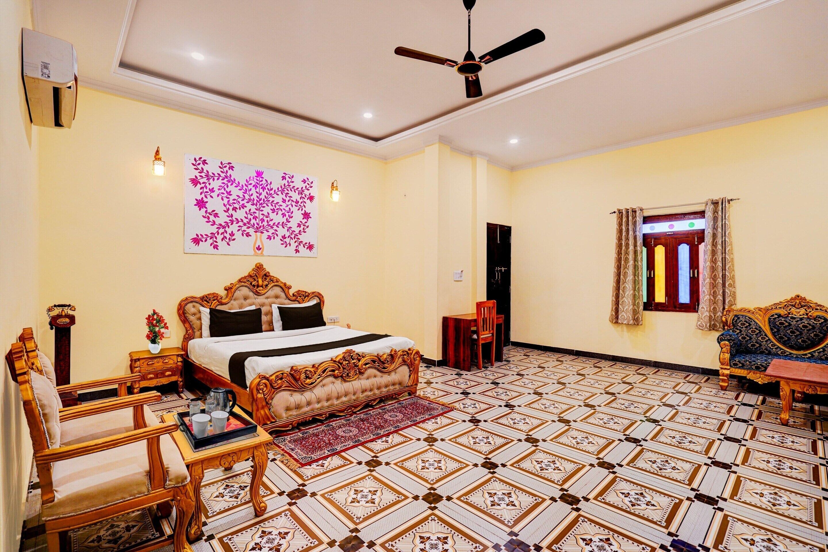 A bedroom with a bed, a chair, a table, a ceiling fan, a wall-mounted light, and a patterned floor.