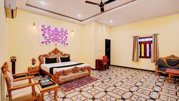 A bedroom with a bed, a chair, a table, a ceiling fan, a wall-mounted light, and a patterned floor.