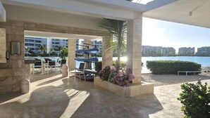 Un espace aménagé au bord de la piscine, avec des chaises longues, une poubelle et une vue sur l’eau et les bâtiments.