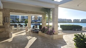 A poolside area with lounge chairs, a trash bin, and a view of the water and buildings. - Beautiful apartment for rent in Punta Cana, the Beach-Cristal Lagoon (Punta Cana)