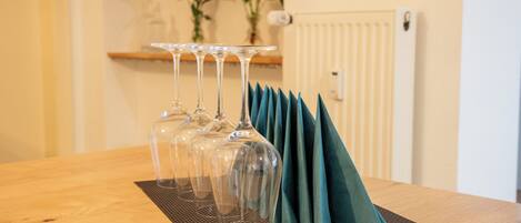 A wooden table with a clear glass wine glass set and a teal napkin holder.