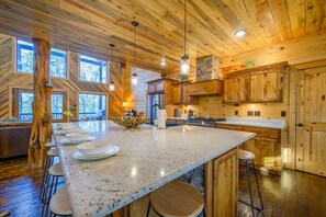 A spacious kitchen with a large island, wooden cabinetry, and a stone fireplace. - Treetops · Sleeps 16: Family Cabin w/ Hot Tub, Games & Decks (Broken Bow)