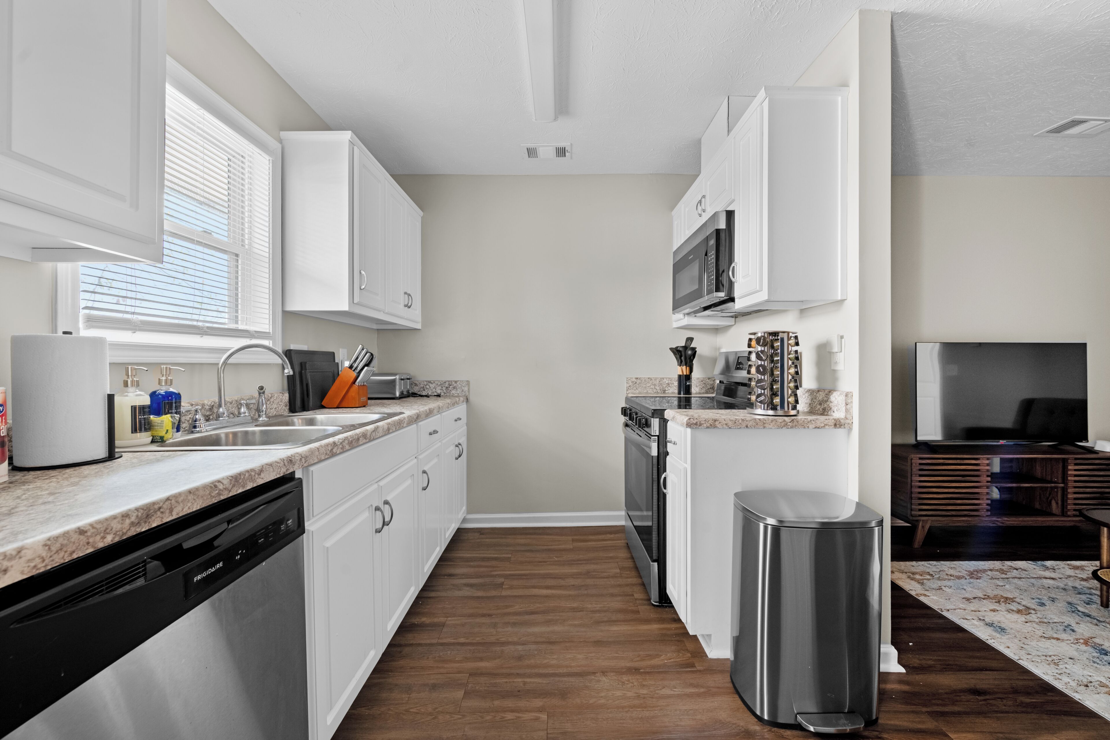 A modern kitchen with white cabinets, a dishwasher, a microwave, and a trash can.