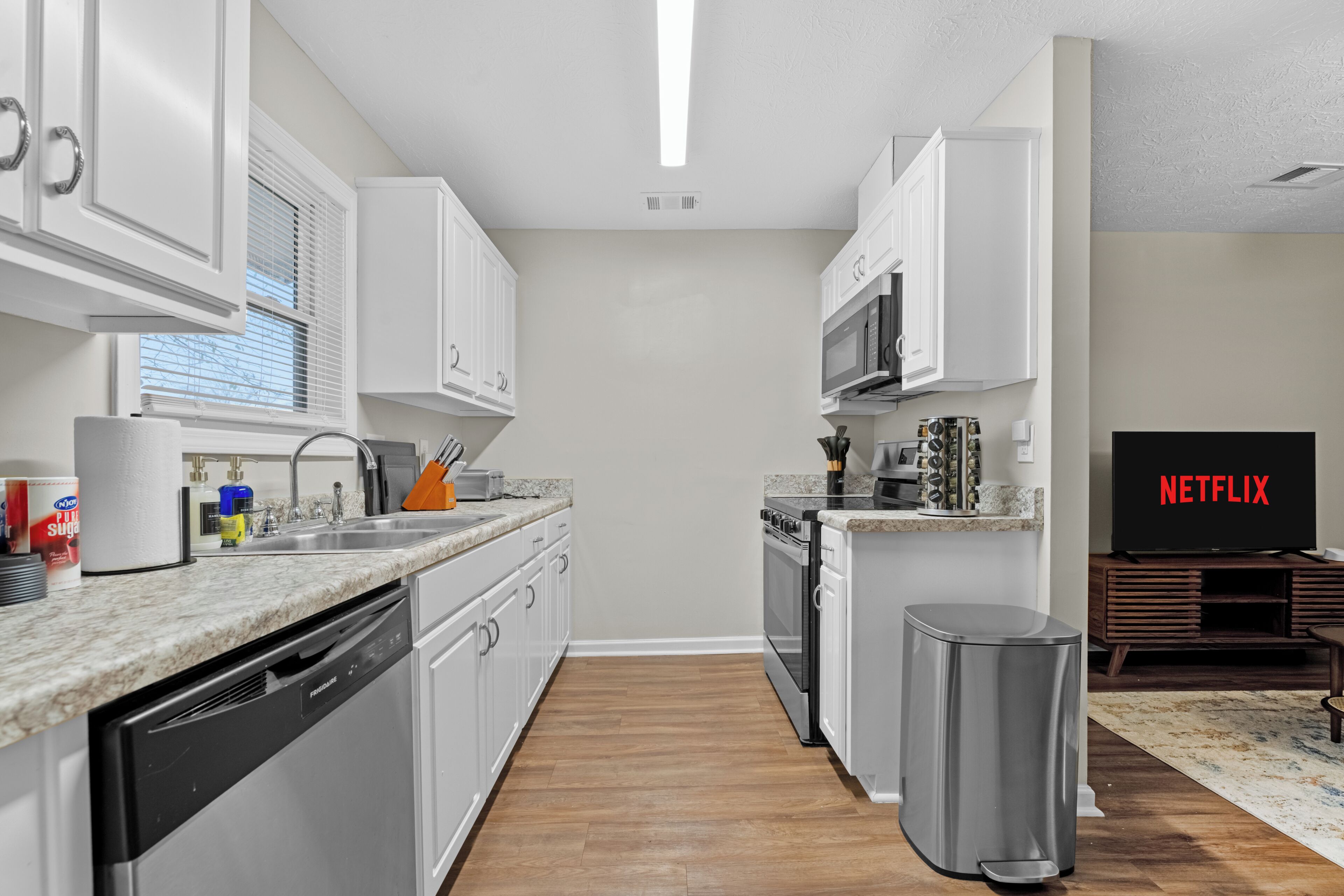 A modern kitchen with white cabinets, a dishwasher, a microwave, and a trash can.