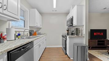 A modern kitchen with white cabinets, a dishwasher, a microwave, and a trash can.
