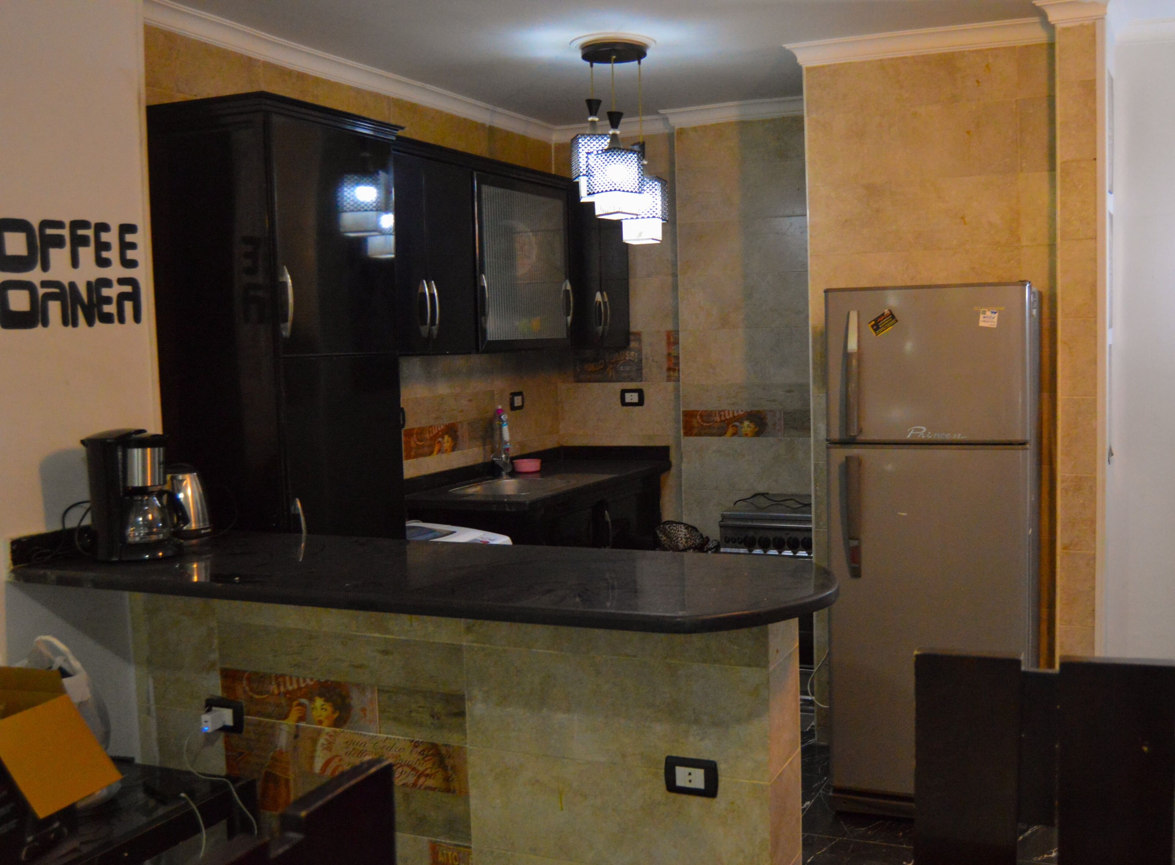 A kitchen with black cabinets, a refrigerator, a coffee maker, and a tiled backsplash.