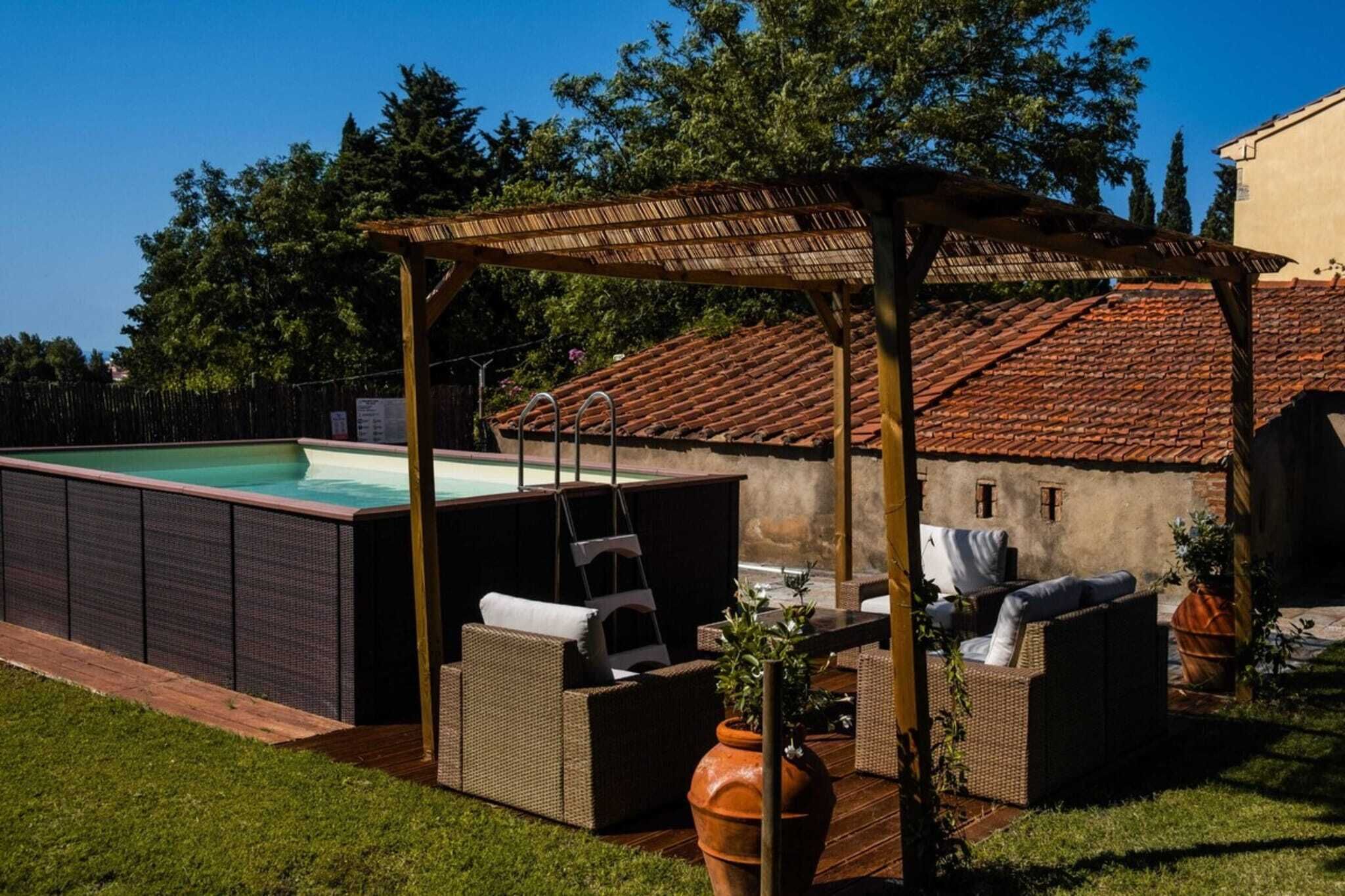 A covered outdoor area with a pool, wicker furniture, and a rustic building with a tiled roof.