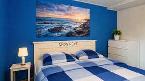 Ein Schlafzimmer mit einem Bett, einem Nachttisch, einer Kommode und einem Gem älde, das einen Sonnenuntergang über dem Meer zeigt.