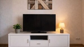 Ein weißes TV-Möbel mit Flachbildfernseher, einer kleinen Topfpflanze und einer Tischlampe.