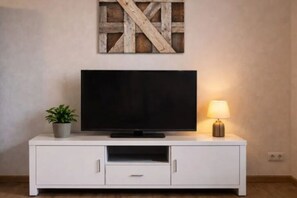 Ein weißes TV-Möbel mit Flachbildfernseher, einer kleinen Topfpflanze und einer Tischlampe.