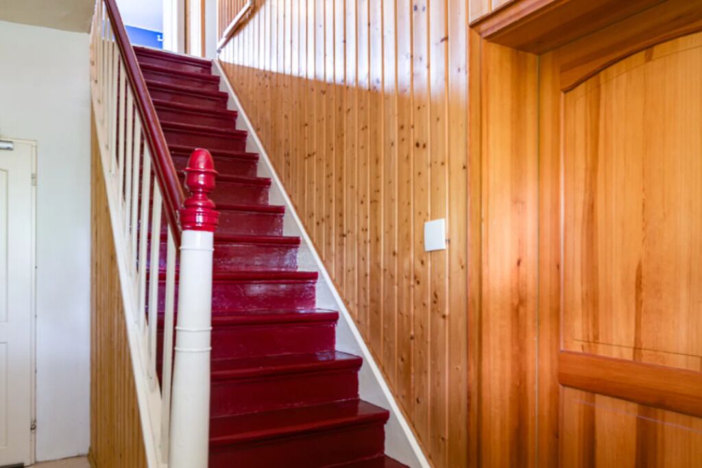 A wooden staircase with red steps and a white handrail.