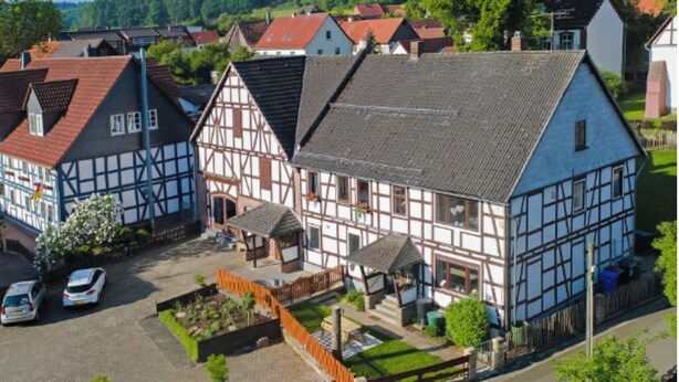 Ein traditionelles Fachwerkhäuschen mit geneigtem Dach, einem kleinen Garten und einer gepflasterten Auffahrt.