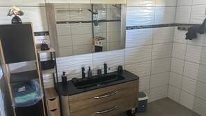 Une salle de bain avec un meuble-lavabo en bois, un lavabo noir, un miroir et un espace douche.