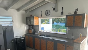 Une petite cuisine équipée d’une cuisinière, d’un évier et de placards, une fenêtre avec vue et une horloge au mur.