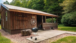 Ein rustikales Holzhaus mit überdachter Veranda, einem Schubkarren und einem Grill.