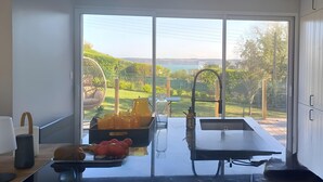 Une cuisine moderne dotée d’une grande porte-fenêtre coulissante qui donne sur un balcon offrant une vue sur un lac et la verdure environnante.
