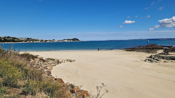 Une plage avec un ciel dégagé, un rivage sablonneux et des affleurements rocheux.