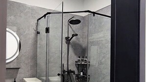 Une salle de bain moderne avec une douche à parois de verre, un lavabo blanc, un miroir et une petite étagère blanche.