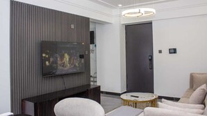 Un salon moderne avec un téléviseur à écran plat fixé au mur, une table basse ronde, un canapé et un luminaire suspendu.