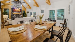 A dining area with a wooden table set for six, surrounded by black chairs, with a stone fireplace and a television mounted on the wall. - moderno farm house getaway-fire pit game room (Culpeper)