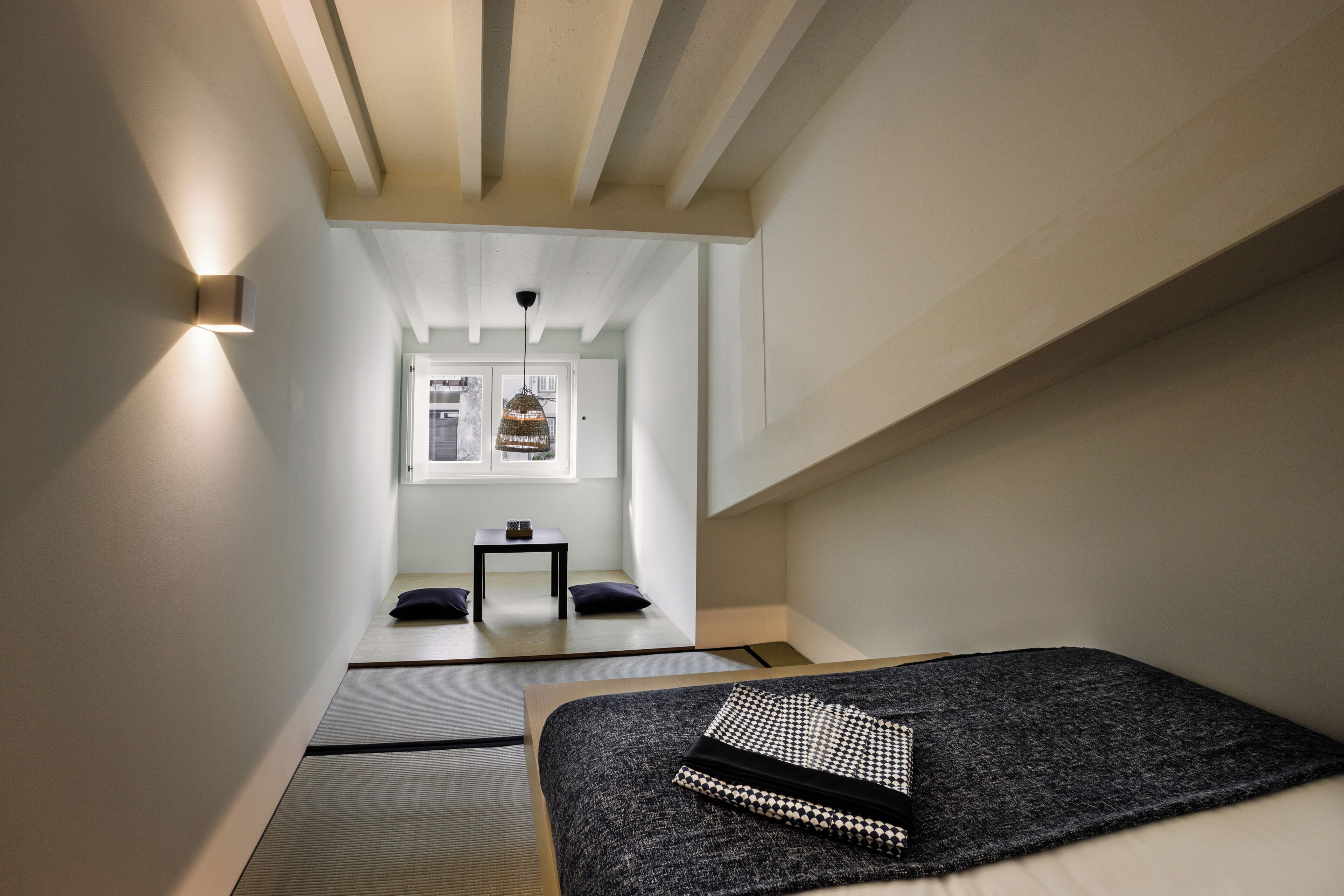 Een strak ingerichte kamer met een bed, een klein tafeltje en een raam.