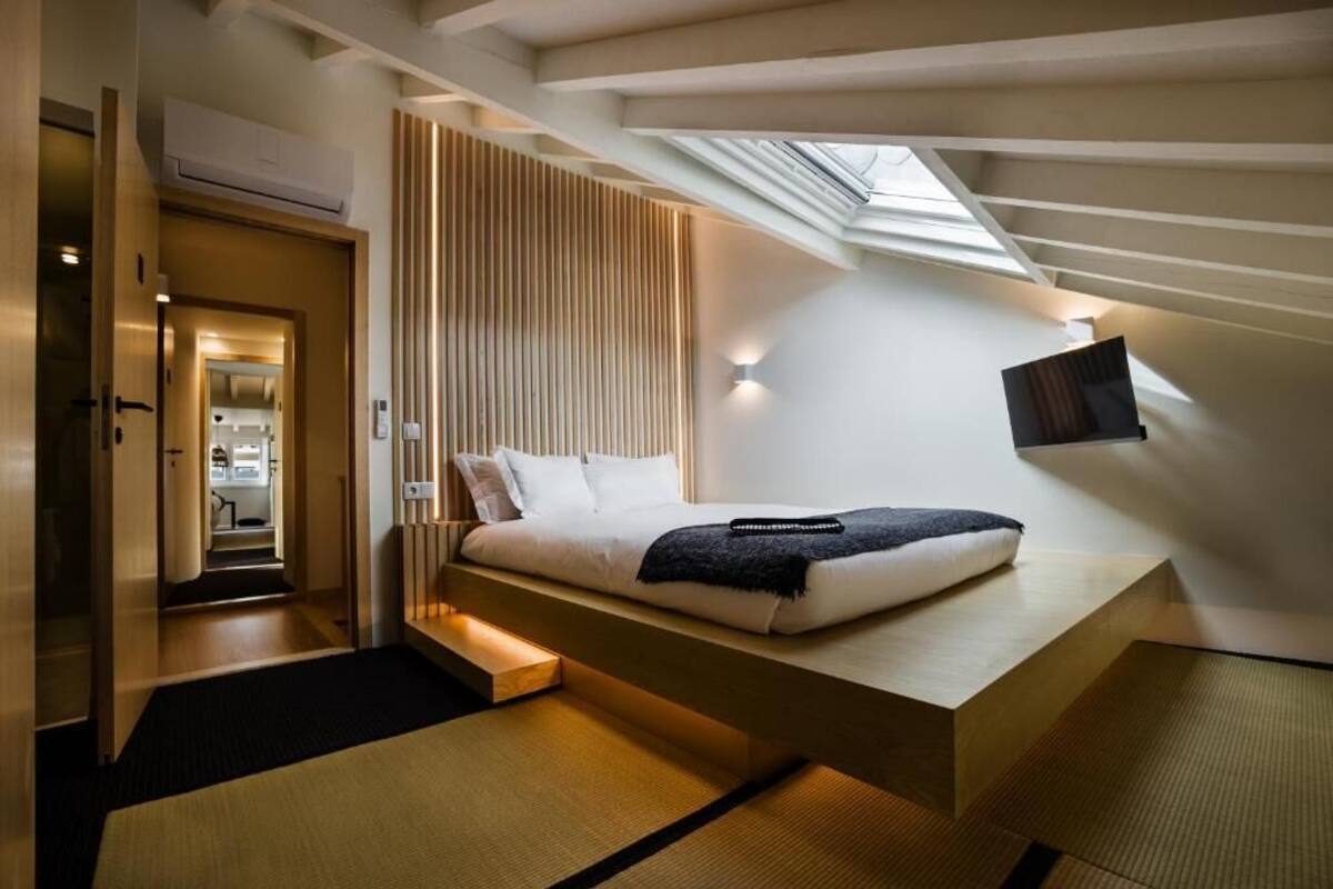 A modern bedroom with a loft bed, a skylight, and a view of the kitchen.