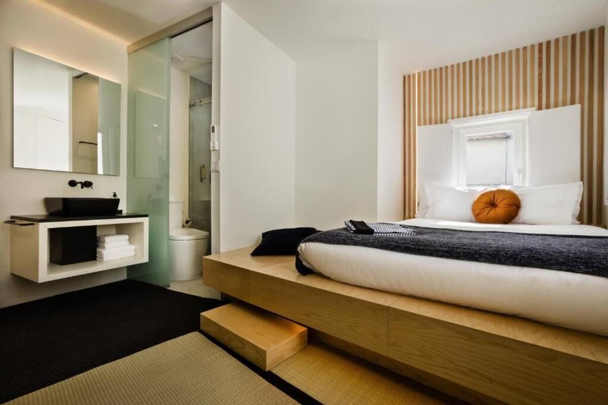 A modern bedroom with a bed, a bedside table, a mirror, and a bathroom with a shower.