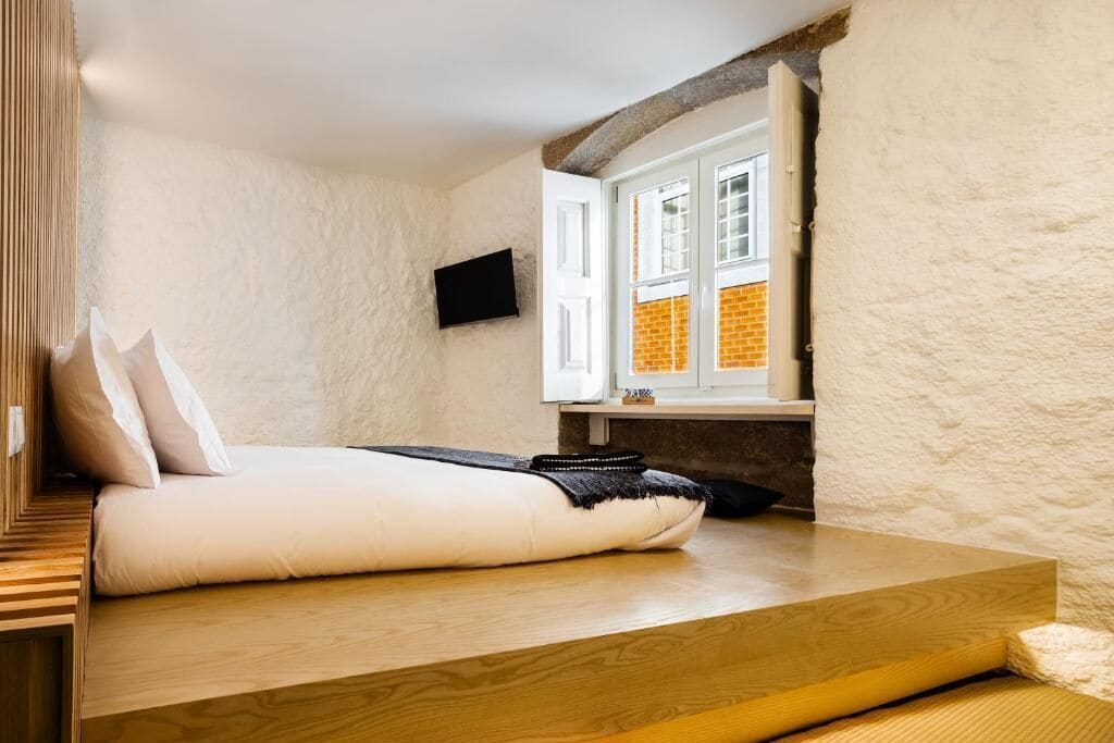 Ein Schlafzimmer mit einem Bett, einem Fernseher, einem Fenster und Blick auf ein Backsteingebäude.